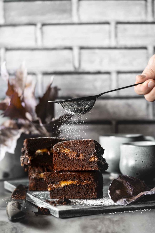 Brownies with melted caramel core Brownies mit flüssigem Karamellkern Kalorienverweigerer, Karamellhasser und Schokoladenzurückweiser bitte wegschauen, denn hier kommt eine Leckerei auf dem Tisch die es in sich hat. Jeder Bissen dieser Brownies schmilzt köstlich in deinem Mund. Die Ränder sind knackig, die Mitte ist „chewy“ und sie haben die perfekte Süße. 1 Springform ca. 20 x 30 cm 250 g Zartbitterschokolade gehackt 250 g Butter 200 g Mehl 1 Pck. Backpulver 100 g Kakaopulver 200 g brauner Zucker 100 g Zucker 1 Prise Salz 2 Päckchen Vanillezucker 8 Eier 200 g Crème fraîche 2 Tafeln Schokolade gefüllt mit Karamell (á 200 g) Puderzucker zum bestäuben Backofen auf 150 Grad Umluft vorheizen Springform mit Backpapier auslegen Schokolade mit der Butter langsam in einem Topf zum schmelzen bringen Mehl, Backpulver, Kakao, braunen Zucker, Zucker, Vanillezucker und Salz vermengen Eier schaumig schlagen, geschmolzene Schokolade unterrühren Mehlmischung zugeben und unterrühren Crème fraîche unterrühren Die Hälfte des Teigs in die Springform geben, Schokolade darauf verteilen, restlichen Teig darüber geben und im Ofen 45 Minuten backen Abkühlen lassen, aus der Form nehmen und auf ein Kuchengitter geben In Stücke schneiden und vor dem Servieren mit Puderzucker bestäuben