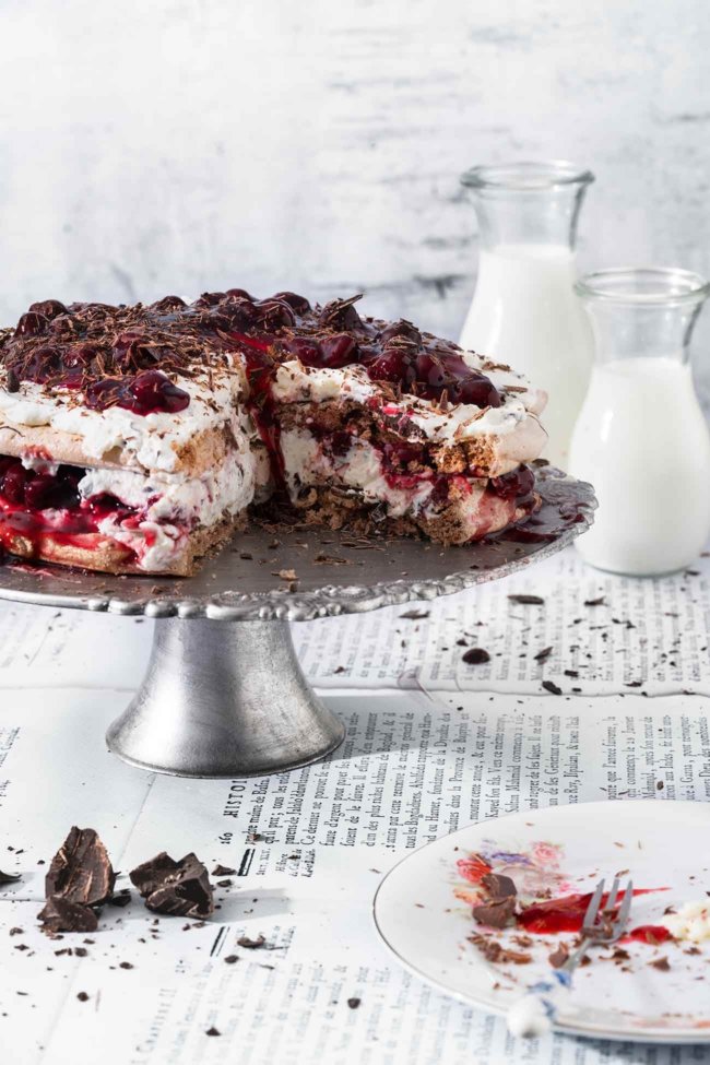 Schwarzwälder Kirsch-Baiser-Kuchen Black Forest cherry meringue cake Schwarzwälder Kirsch bleibt und ist einfach ein richtig guter Kuchenklassiker. Ich mag manchmal einfach keine Tortenböden backen, so dass ich kurzerhand die Biskuitböden gegen leckere Schokoladenbaisers ersetzt habe. Geht unheimlich flott und ist ab sofort unsere Lieblingsversion der Schwarzwälder Kirschtorte. 5 Eiweiß 1 TL Essig 200 g Zucker 2 TL Speisestärke 3 EL Kakaopulver 200 g Zartbitterkuvertüre 600 g Schlagsahne 3 Blatt Gelatine 600 g Sauerkirschen (Glas) 50 g brauner Zucker 2 Pck. Vanillezucker 50 ml Kirschwasser 6 TL Sofortgelatinepulver (weniger als 1 Pck) Backofen auf 140 Grad Ober-Unterhitze vorheizen und zwei Backbleche mit Backpapier auslegen Eiweiße mit dem Essig steif schlagen Zucker mit der Speisestärke vermengen und nach und nach einrieseln lassen Kakaopulver unterheben Auf den Backpapieren einen Teller mit 22 cm Durchmesser legen und nachzeichnen Eiweißmasse in einen Spritzbeutel geben und die beiden Kreise ausspritzen Die Böden ca. 1,5 Stunden im Backofen backen, danach auskühlen lassen 100 g Zartbitterkuvertüre über einem Wasserbad schmelzen lassen und die Baiserböden damit einpinseln, trocknen lassen Blattgelatine in kaltem Wasser einweichen Sauerkirschen abseihen und 200 ml Saft auffangen 150 ml Saft mit dem braunen Zucker und den Kirschen verrühren, restlichen Saft mit der Speisestärke verrühren Kirschen mit Saft in einen Topf geben und aufkochen lassen und mit der Speisestärkemischung binden Kirschkompott abkühlen lassen Sahne, Vanillezucker, Kirschwasser und Sofortgelatinepulver steif schlagen Restliche Kuvertüre raspeln und 2/3 unter die Sahne heben Einen Baiserboden mit Sahne und Kirschkompott bestreichen, zweiten Boden auflegen und restliche Sahne darauf verteilen Restlichen Kompott und Schokoraspeln darauf verteilen TIPP: Wer das Kirschwasser weglassen will, kann die Sahne auch mit Sahnesteif steif schlagen und benötigt keine Sofortgelatine