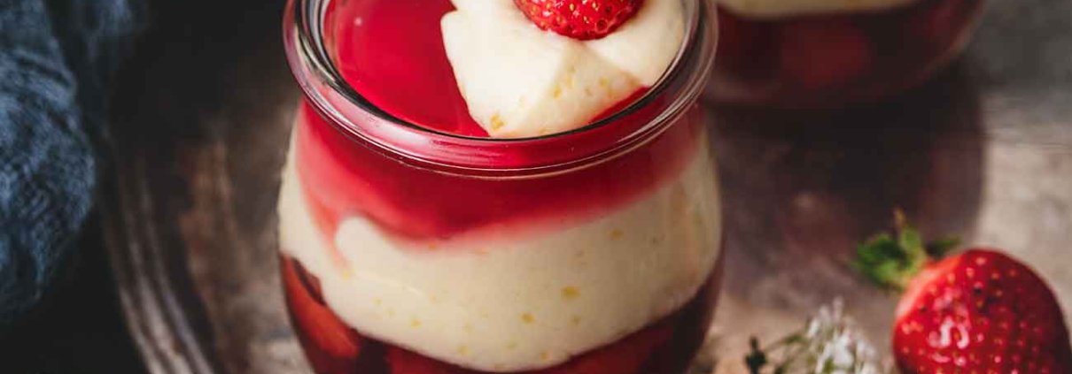Götterspeise mit Orangen-Vanillepudding und Erdbeeren Jelly with orange custard and strawberries Jetzt wird es fruchtig im Glas: Himbeer, Erdbeer und Orange! Den Wunsch „ich möchte mal wieder Götterspeise essen“ habe ich erfüllt. Ich finde Götterspeise ehrlich gesagt ja ziemlich langweilig, aber in dieser Kombination finde ich sie richtig klasse. 4 Portionen 1 Beutel Himbeer Instant Götterspeisenpulver für 500 ml Wasser 1 Pck. Vanille-Puddingpulver zum Kochen 500 ml Orangensaft 100 g Zucker 300 ml Schlagsahne 250 g Erdbeeren, gewürfelt Puddingpulver mit dem Zucker und 6 EL Orangensaft verrühren Restlichen Saft aufkochen, angerührtes Puddingpulver zugeben und aufkochen lassen Eine Minute köcheln lassen, auskühlen lassen, dabei ab und zu umrühren 500 ml kochendes Wasser mit dem Instant Götterspeisenpulver verrühren und ca. die Hälfte der Flüssigkeit auf 4 Gläser aufteilen Erdbeerwürfel zugeben und kalt stellen 2/3 der Orangen-Vanillepudding auf die Gläser verteilen, danach die restliche Götterspeise darüber gießen, gefolgt von dem restlichen Pudding Alles im Kühlschrank fest werden lassen