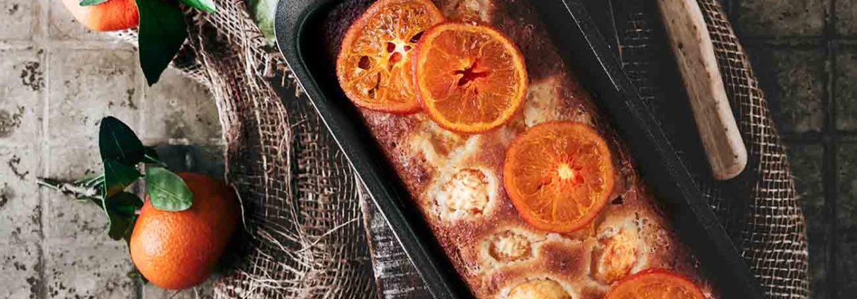 Mandarinen-Orangen Joghurt Kuchen Tangerine Orange Yoghurt Cake Dieser super softe Winter-Citrus Kuchen, mit einer Mischung aus Orangen und Mandarinen ist irgendwie warm und beruhigend. Ein toller Kuchen für das stürmische Wetter da draußen. 2 Orangen 4 Mandarinen 1 TL Vanilleextrakt 300 g Mehl 3 TL Backpulver 1 Prise Salz 500 g Zucker 150 g Joghurt (Vanille oder Natur) 5 Eier 150 g Olivenöl Orangen heiß abwaschen und die Schale fein abreiben, Saft auspressen und 200 ml Saft auffangen Saft und 200 ml Zucker in einen Topf geben und zum Kochen bringen, bis sich der Zucker vollständig aufgelöst hat Zwei Mandarinen mit Schale in feine Scheiben schneiden, dann zur Zuckermischung geben und 5 Minuten mit köcheln lassen Backofen auf 120 Grad Ober-Unterhitze vorheizen, Mandarinenscheiben entnehmen, abtropfen lassen und auf ein mit Backpapier ausgelegten Backblech legen und im Ofen 60 Minuten backen Backofen auf 180 Grad Ober-Unterhitze und eine Kastenform (Länge ca. 25 cm) mit Backpapier auslegen Orangenschale mit dem restlichen Zucker vermengen Eier mit Joghurt, Vanille und Olivenöl aufschlagen Mehl, Backpulver und Salz vermengen und nach und nach unterrühren Teig in die Form geben Restliche Mandarinen schälen und die einzelnen Mandarinenstükchen auf den Teig geben und ganz leicht andrücken Im Ofen 50-60 Minuten backen (Stäbchenprobe machen) und komplett in der Form auskühlen lassen Vor dem Servieren mit den kandierten Mandarinenscheiben und/oder dem restlichen Sirup beträufeln