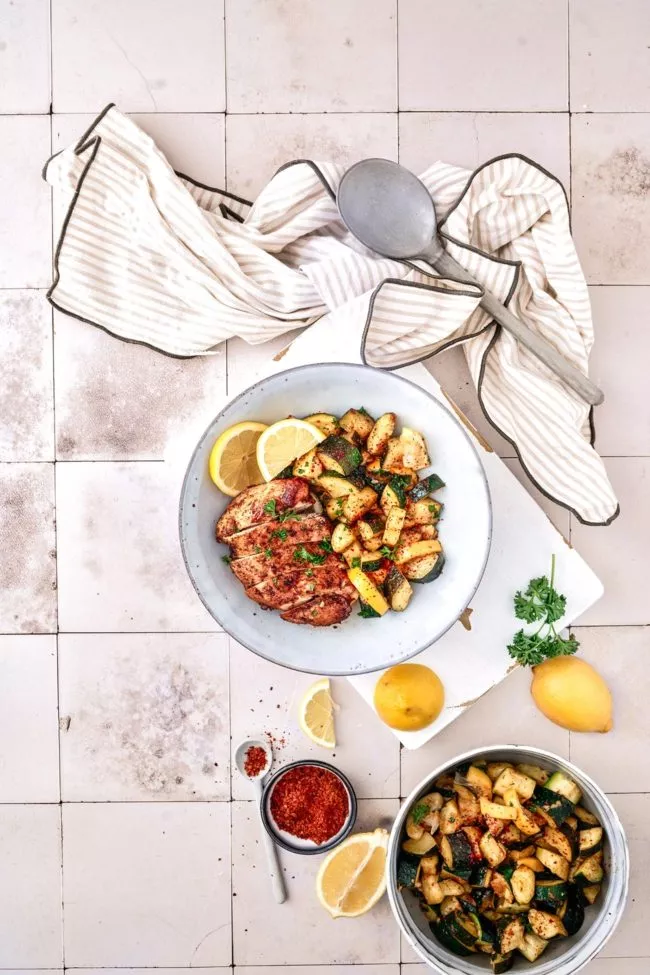 Hähnchenbrust mit sautierter Zitronen-Zucchini Für 4 Portionen 1 EL Paprikapulver 2 TL gemahlener Kümmel 60 ml Hühnerbrühe 60 ml Zitronensaft ½ TL gemahlenes Zwiebelpulver 2 TL Oregano 8 Knoblauchzehen, gehackt ½ TL Chiliflocken 60 ml Olivenöl Salz Pfeffer Sonnenblumenöl 1,2 kg Hähnchenbrust 5 Zucchini, gewürfelt 2 Bio-Zitronen, in Scheiben geschnitten und in geviertelt 1 Bio-Zitrone, in Scheiben geschnitten ½ Bund Petersilie, gehackt Paprika, Kreuzkümmel, Hühnerbrühe, Zitronensaft, Zwiebelpulver, Oregano, Knoblauch, Chiliflocken und Olivenöl in einer Schüssel vermengen und mit Salz und Pfeffer würzen. Hähnchenbrust von allen Seiten mit der Marinade bestreichen, dann ganz in die Marinade geben und mindestens 30 Minuten im Kühlschrank zugedeckt ziehen lassen. Etwas Sonnenblumenöl in einer Pfanne bei mittlerer Hitze erhitzen, die Hähnchenbrust aus der Marinade nehmen und von beiden Seiten ca. 15 Minuten braten. Hähnchenbrust auf einen Teller geben und warm halten. Zucchini in dieselbe Pfanne geben und mit Salz, Pfeffer und roten Chiliflocken würzen, bei Bedarf etwas Öl hinzufügen. Zucchini für 3 Minuten bei mittlerer Hitze sautieren, dann etwas Marinade und die Zitronenviertel zugeben. Unter Rühren 3-4 Minuten köcheln lassen. Zucchini mit in Scheiben geschnittener Hähnchenbrust auf Teller verteilen und mit der gehackten Petersilie und Zitronenscheiben servieren.
