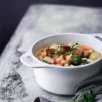 Minestrone aus dem Ofen Oven minestrone Diese Minestrone aus dem Ofen ist die perfekte Schüssel zum Aufwärmen an kalten Herbst-und Wintertagen. Jede Portion wird getoppt mit knusprigen Parmesan-Croutons und frischer Petersilie. Diese Schüssel Minestrone ist eine gemütliche Mahlzeit, bei der man sich einfach wohlfühlen muss. 1,5 Liter Gemüsebrühe 1 Zwiebel, gewürfelt 2 Möhren, gewürfelt ¼ Knollensellerie, gewürfelt 300 g Wirsing, in Streifen geschnitten 1 Lauch, halbiert und in Ringe geschnitten 2 Knoblauchzehen, gehackt 3 Tomaten, gewürfelt 400 g weiße Bohnen, aus der Dose 100 g Pasta ½ Bund Petersilie 200 g Bauernbrot, gewürfelt 25 g Parmesan, gerieben 1 EL Butter Backofen auf 200 Grad Ober-Unterhitze vorheizen. Gemüsebrühe in einen ofenfesten Topf zum Kochen bringen. Zwiebel. Möhren, Sellerie, Wirsing, Lauch, Knoblauch, Tomaten, Bohnen und Pasta in den Topf geben und alles 50 Minuten mit geschlossenem Deckel garen. In der Zwischen die Butter in einer Pfanne erhitzen und die Brotwürfel anbraten, Parmesan darüberstreuen. Suppe mit Croutons und Petersilie servieren.