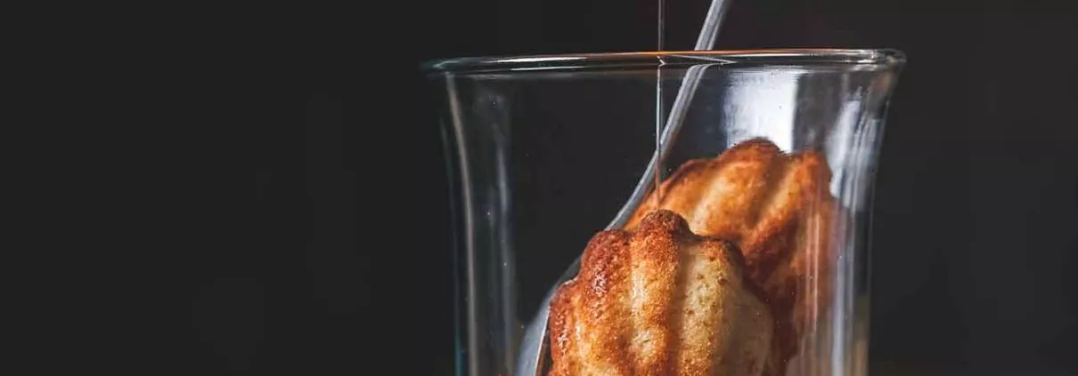 Madeleines im Glas mit Rum-Sirup Madeleines in a glass with rum syrup Madeleines gehören für mich zu den leckersten kleinen Kuchen der Welt. Nun ja, wenn sie eben genau so gemacht wurden, wie in diesem Rezept. Das Rezept der Madeleines habe ich von Lea Linster erhalten, nach ein paar Flaschen Champagner als alle anderen Gäste schon weg waren. Noch lange bevor es in Bücher veröffentlicht wurde. Genau so müssen Madeleines schmecken. Vorsicht: Sie machen süchtig. Wichtig ist es, den Teig einen Tag vorher zuzubereiten und über Nacht ruhen zu lassen. Und weil Madeleines so lecker sind, werden sie jetzt auch zum Lieblingsdessert im Glas, mit einem Rum-Vanille Sirup. Für 4 Portionen Madeleines 80 g Butter 3 Eiweiß 100 g Puderzucker 60 g Mehl 40 g gemahlene Mandeln 1 TL Honig 1 Messerspitze Backpulver Rum-Sirup 150 ml Wasser 200 g Zucker 200 ml brauner Rum 1 TL Vanilleextrakt Für den Sirup das Wasser mit dem Zucker in einen Topf geben und leicht erhitzen, bis sich der Zucker vollständig aufgelöst hat. Dann unter Rühren 5 Minuten köcheln lassen, bis alles eine goldbraune Farbe angenommen hat und leicht eingedickt ist. Dann langsam den Rum und Vanille unterrühren. Auskühlen lassen. Für die Madeleines Butter erhitzen, bis sie leicht bräunlich wird und leicht nussig riecht. Eiweiß sehr steif schlagen. Puderzucker(gesiebt), Mehl (gesiebt) und Mandeln vermengen und mit dem Honig und der Butter unter das Eiweiß heben. Teig eine Nacht im Kühlschrank ruhen lassen. Am nächsten Tag, vor dem Backen, das Backpulver unterrühren. Backofen auf 180 Grad vorheizen. Madeleine-Formen mit Butter einfetten und mit Mehl bestäuben. Den Teig mit einem kleinen Löffel in die Madeleine-Form geben. 10 -15 Minuten backen, bis sie schön goldbraun werden. Je nach Größe 3-4 Madeleines in ein Glas geben und mit dem Sirup begießen. Am besten 2 Minuten warten, bis sich die Madeleines mit etwas Sirup vollgesogen haben. TIPP: Zu den Madeleines im Glas passt etwas Sahne. Noch ein TIPP: Ich bereite immer direkt eine ganze Ladung an Madeleines zu. Sie lassen sich perfekt einfrieren und können kurz aufgebacken werden.