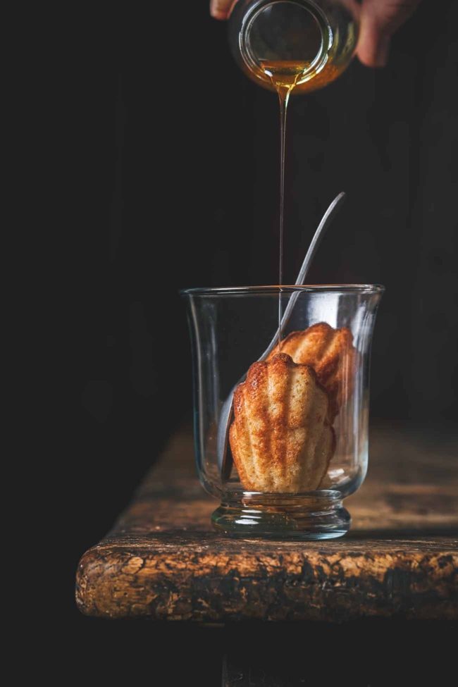 Madeleines im Glas mit Rum-Sirup Madeleines in a glass with rum syrup Madeleines gehören für mich zu den leckersten kleinen Kuchen der Welt. Nun ja, wenn sie eben genau so gemacht wurden, wie in diesem Rezept. Das Rezept der Madeleines habe ich von Lea Linster erhalten, nach ein paar Flaschen Champagner als alle anderen Gäste schon weg waren. Noch lange bevor es in Bücher veröffentlicht wurde. Genau so müssen Madeleines schmecken. Vorsicht: Sie machen süchtig. Wichtig ist es, den Teig einen Tag vorher zuzubereiten und über Nacht ruhen zu lassen. Und weil Madeleines so lecker sind, werden sie jetzt auch zum Lieblingsdessert im Glas, mit einem Rum-Vanille Sirup. Für 4 Portionen Madeleines 80 g Butter 3 Eiweiß 100 g Puderzucker 60 g Mehl 40 g gemahlene Mandeln 1 TL Honig 1 Messerspitze Backpulver Rum-Sirup 150 ml Wasser 200 g Zucker 200 ml brauner Rum 1 TL Vanilleextrakt Für den Sirup das Wasser mit dem Zucker in einen Topf geben und leicht erhitzen, bis sich der Zucker vollständig aufgelöst hat. Dann unter Rühren 5 Minuten köcheln lassen, bis alles eine goldbraune Farbe angenommen hat und leicht eingedickt ist. Dann langsam den Rum und Vanille unterrühren. Auskühlen lassen. Für die Madeleines Butter erhitzen, bis sie leicht bräunlich wird und leicht nussig riecht. Eiweiß sehr steif schlagen. Puderzucker(gesiebt), Mehl (gesiebt) und Mandeln vermengen und mit dem Honig und der Butter unter das Eiweiß heben. Teig eine Nacht im Kühlschrank ruhen lassen. Am nächsten Tag, vor dem Backen, das Backpulver unterrühren. Backofen auf 180 Grad vorheizen. Madeleine-Formen mit Butter einfetten und mit Mehl bestäuben. Den Teig mit einem kleinen Löffel in die Madeleine-Form geben. 10 -15 Minuten backen, bis sie schön goldbraun werden. Je nach Größe 3-4 Madeleines in ein Glas geben und mit dem Sirup begießen. Am besten 2 Minuten warten, bis sich die Madeleines mit etwas Sirup vollgesogen haben. TIPP: Zu den Madeleines im Glas passt etwas Sahne. Noch ein TIPP: Ich bereite immer direkt eine ganze Ladung an Madeleines zu. Sie lassen sich perfekt einfrieren und können kurz aufgebacken werden.