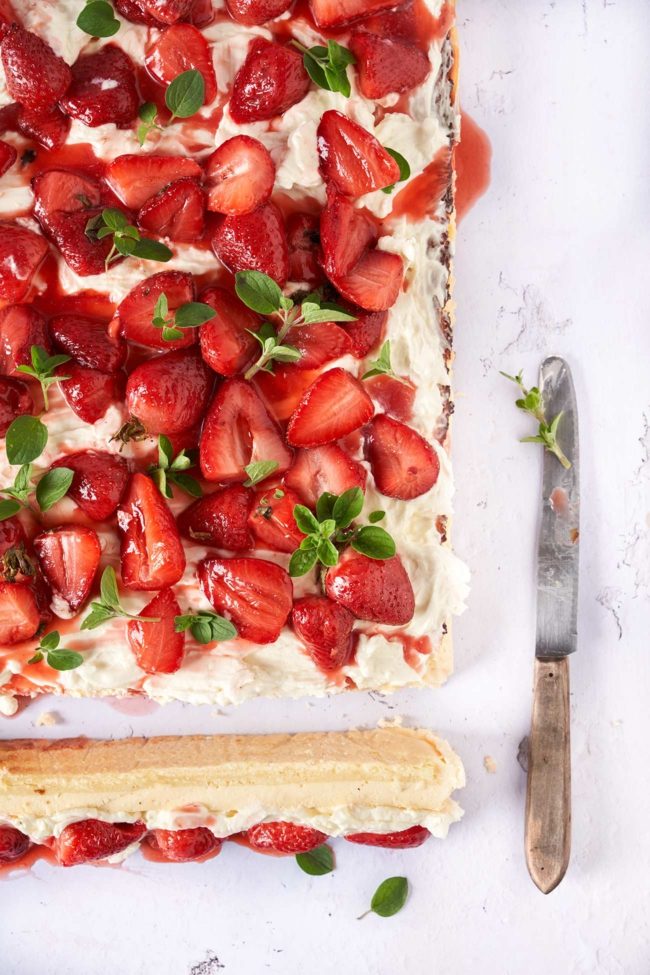 Der Blechkuchen mit gerösteten Erdbeeren lässt mir noch beim Schreiben das Wasser im Mund zusammenlaufen. Wenn du die Erdbeeren mit Honig und Thymian röstest, entsteht ein köstlicher Erdbeersirup, der den Kuchen perfekt ergänzt. Dieser Blechkuchen besteht aus drei unwiderstehlichen Schichten, die jeden Bissen zu einem Genuss machen. Die erste Schicht ist der Boden, mit leichtem Orangengeschmack.Dieser Boden bildet die perfekte Grundlage für den Kuchen und bietet einen angenehmen Kontrast zu den cremigen Toppings. Die zweite Schicht ist die verlockende Käsekuchenfüllung mit Frischkäse und cremigen Ricotta, die im Ofen gebacken wird. Die dritte Schicht ist eine Creme aus Mascarpone und frischer Sahne und den gerösteten Honig-Erdbeeren. Der Honig karamellisiert leicht und verleiht den Erdbeeren eine süße Note, während der Thymian einen subtilen Hauch von Kräutern hinzufügt. Verteile die gerösteten Erdbeeren auf dem gebackenen Käsekuchen und beträufle ohn mit dem entstandenen Erdbeersirup.