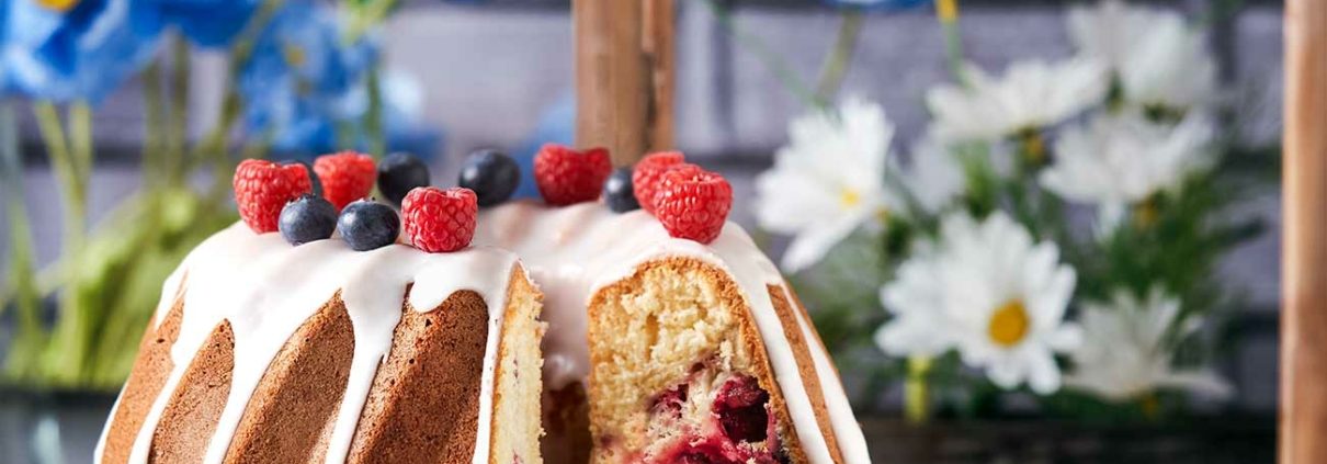 Beeren Gugelhupf mit Glasur vor einem Küchenfenster