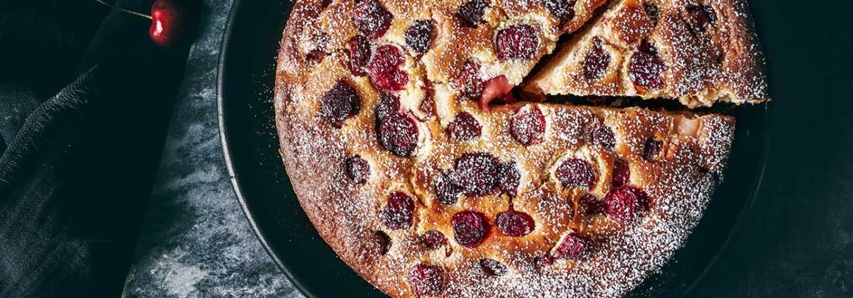 Kirschkuchen auf einem Tisch mit Kirschen drumherum