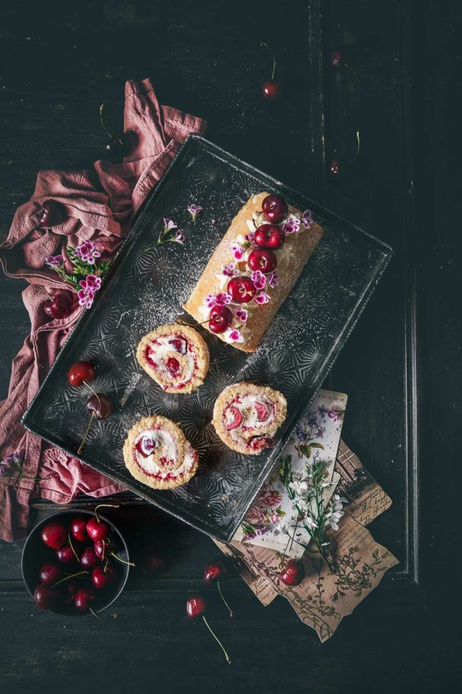 Biskuitrolle auf einem dunklen Holztisch. Biskuitrolle ist gefüllt mit Kirschen und Marmelade
